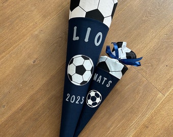 Peut inclure: Deux cônes d'école bleus et blancs avec des motifs de ballon de football. Le plus grand cône porte le nom "LIO" et l'année "2023" imprimée dessus. Le plus petit cône porte le nom "MATS" imprimé dessus.