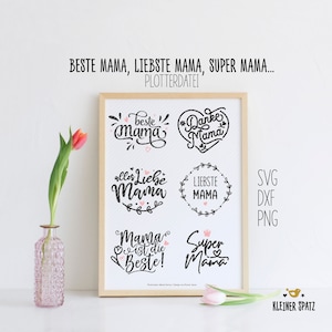 Könnte beinhalten: Ein gerahmter Druck mit fünf verschiedenen Designs, die das Wort "Mama" in verschiedenen Stilen zeigen. Die Designs beinhalten "Beste Mama", "Danke Mama", "Alles Liebe Mama", "Liebste Mama" und "Mama ist die Beste!" mit einer Krone über dem Wort "Mama". Der Druck enthält auch den Text "Super Mama" mit einem Herzen. Der Druck ist von einem Holzrahmen umgeben und befindet sich auf einer weißen Oberfläche.