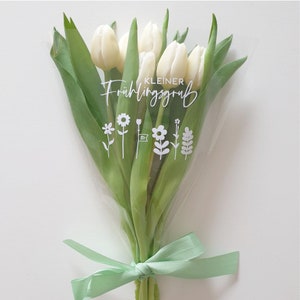Peut inclure: Un bouquet de tulipes blanches envelopp&eacute; dans du cellophane transparent avec un ruban vert. Le bouquet porte une &eacute;tiquette blanche avec le texte "KLEINER Fr&uuml;hlingsgru&szlig;" et un petit graphique de fleurs.