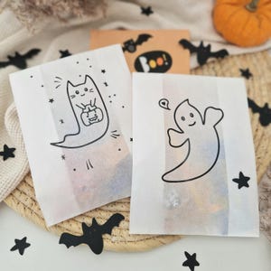 May include: Two white paper bags with black Halloween-themed illustrations. One bag features a ghost holding a heart and the other features a cat dressed as a ghost holding a pumpkin.