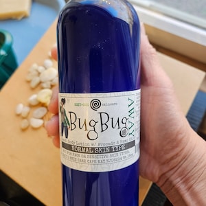 May include: A blue plastic bottle of BugBug body lotion with avocado and hemp oil. The bottle is labeled for normal skin type and states it is not for face or sensitive skin types. The bottle is 16 oz.