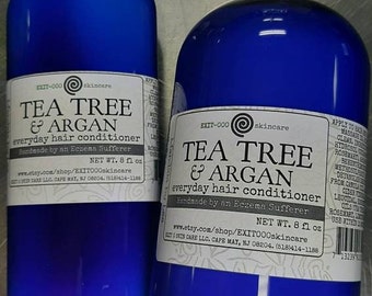 May include: Two blue bottles of Tea Tree & Argan everyday hair conditioner, handmade by an eczema sufferer. Each bottle has a white label with the product name, ingredients, and website information. The bottles are 8 fluid ounces each.