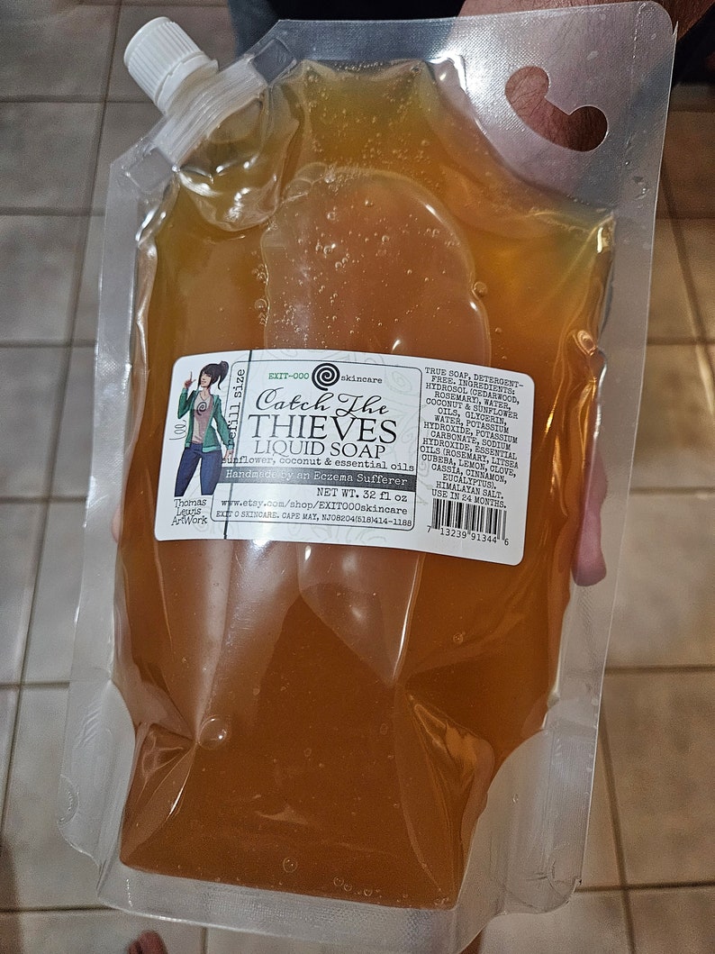 May include: A transparent pouch containing amber liquid soap. The label reads "Catch The Thieves Liquid Soap" and includes a cartoon illustration. The pouch has a white spout for dispensing. The label also lists ingredients.