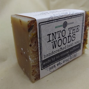 May include: A bar of handcrafted bath soap labeled "Into the Woods" made by an eczema sufferer. The soap is a light brown color and has a natural, earthy scent. It weighs 4 ounces.