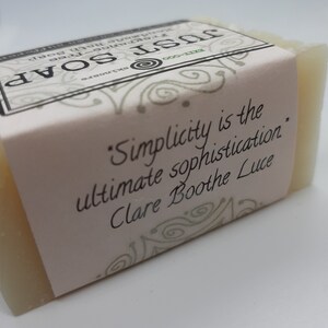 May include: A rectangular bar of handmade soap with a pale colour. The soap is wrapped with a light pink label. The label features the text "Simplicity is the ultimate sophistication" by Clare Boothe Luce, along with the words "JUST SOAP" and "fragrance-free".