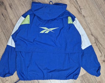 May include: A blue, white, and green windbreaker jacket with a Reebok logo on the front. The jacket has a hood and a zipper closure.