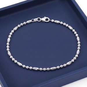 May include: A silver-toned chain bracelet featuring an alternating pattern of small, textured spherical beads and elongated, cylindrical bar beads. The bracelet is secured with a polished lobster claw clasp, creating a continuous circular loop.
