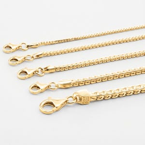 Puede incluir: Primer plano de cinco collares de cadena dorados con cierres de mosquetón. Las cadenas tienen un diseño tejido y texturizado. Un cierre está estampado con "ITALY 925". Los collares se muestran sobre un fondo blanco.