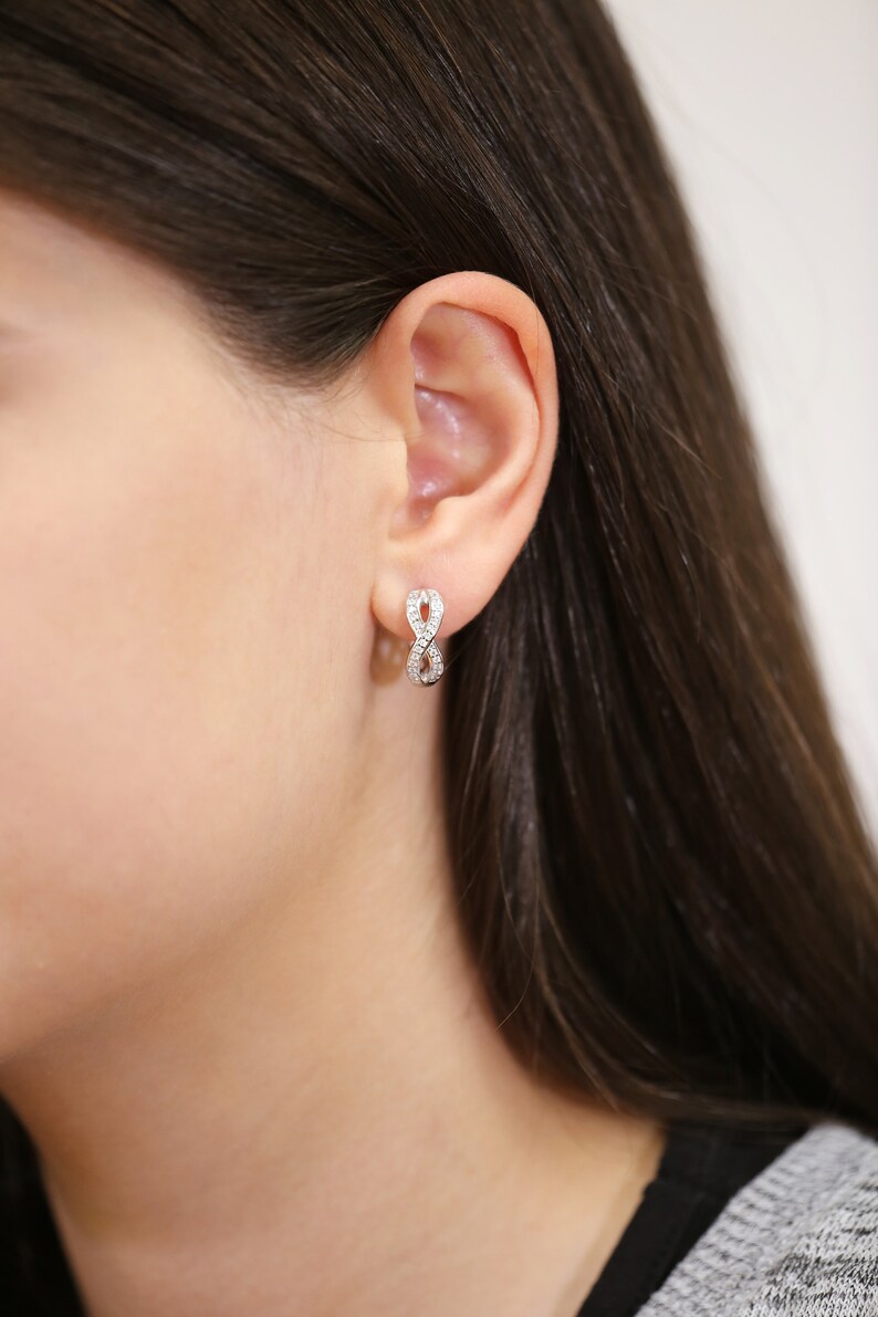 May include: A pair of silver infinity earrings with small clear cubic zirconia stones.