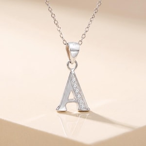 May include: A silver-toned necklace featuring a pendant shaped like the capital letter A. The pendant is suspended from a delicate chain and is accented with a vertical row of small, clear, sparkling stones along the right side of the letter.