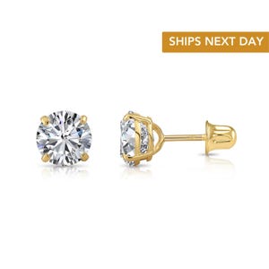 May include: A pair of gold stud earrings with a large, clear, round-cut gemstone. The earrings have a classic four-prong setting and a post with a butterfly backing. The image includes the text "SHIPS NEXT DAY".