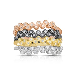 May include: A stack of five rings in various metal tones: rose gold, black, yellow gold, and silver. Each ring features a wavy design adorned with small, sparkling stones, creating a textured, eye-catching look. The rings are stacked together.