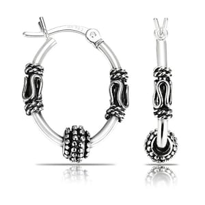 May include: Silver hoop earrings with a textured ball charm and intricate detailing. The earrings have a hinged closure.