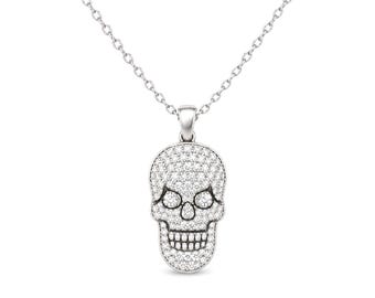 Puede incluir: Un collar de tono plateado con un colgante en forma de calavera. Toda la superficie de la calavera está incrustada con numerosas piedras pequeñas, claras y brillantes, mientras que las cuencas de los ojos y los dientes están definidos por bordes de metal pulido.