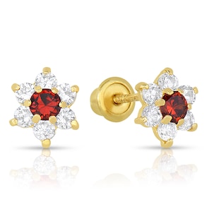 Puede incluir: Un par de pendientes de oro en forma de flor con una piedra preciosa roja en el centro y piedras de circonita cúbica transparentes alrededor de la piedra preciosa. Los pendientes tienen un cierre de rosca.