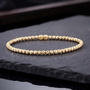 May include: A gold-toned beaded bracelet featuring small, textured, spherical beads arranged in a continuous circular band. The clasp area is marked with the text 925 and ITALY, indicating the metal composition and origin of this jewellery piece.