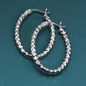 May include: A pair of silver oval hoop earrings with a textured, diamond-shaped design.