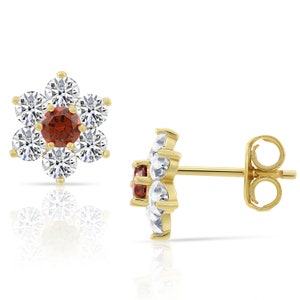 May include: A pair of gold flower-shaped earrings with a red gemstone in the center and clear cubic zirconia stones around it.