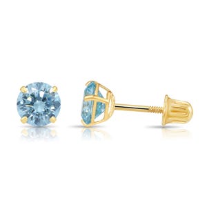 May include: A pair of gold stud earrings with light blue gemstones. The earrings feature a round, light blue gemstone held in place by four prongs. The post and backing are gold. The earrings are displayed on a white background.