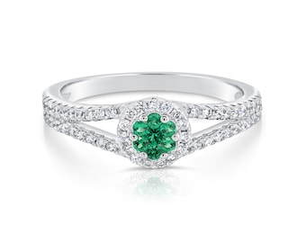 Puede incluir: Un anillo de plata con una esmeralda verde rodeada por un halo de diamantes más pequeños. El anillo tiene una banda dividida con diamantes engastados a lo largo de la banda.