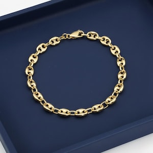 May include: A gold-colored bracelet with a coffee bean link design. The bracelet is made of shiny metal and has a lobster clasp closure. The bracelet is displayed on a dark blue surface.