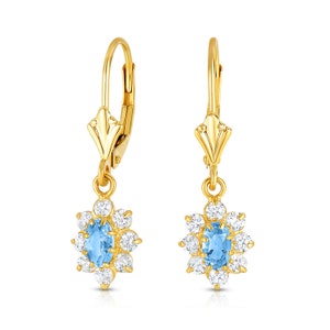 May include: A pair of gold dangle earrings with a blue oval gemstone surrounded by smaller clear gemstones. The earrings have a lever back closure.