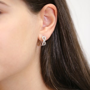 May include: A pair of silver hoop earrings with a diamond-like design. The earrings are worn in the ear of a person with long brown hair.