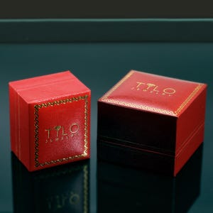 May include: Two red jewelry boxes with gold trim and the text "Tilo Jewelry" on the top.