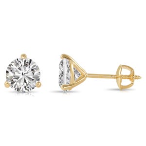 May include: A pair of diamond stud earrings with a classic three-prong setting. The round-cut diamonds sparkle against the yellow gold posts and backs. One earring is shown from the front, and the other is shown from the side.