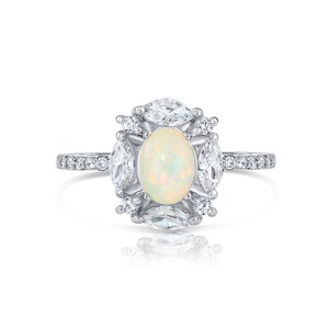 May include: A silver-toned ring featuring a central oval-shaped iridescent opal gemstone. The opal is surrounded by four marquise-cut clear stones and four small round clear stones. The band is thin and accented with small clear stones along the sides.