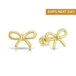 May include: A pair of gold-colored bow-shaped stud earrings. The earrings are displayed on a white background. The text "SHIPS NEXT DAY" is in a gold rectangle in the upper right corner.