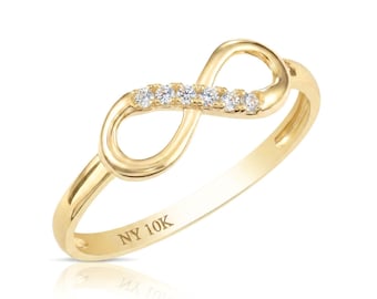 Puede incluir: Un anillo de oro amarillo de 10K con un diseño de símbolo de infinito en la parte superior. El bucle del infinito está adornado con cinco pequeñas piedras redondas y transparentes engastadas a lo largo de un lado. El interior lleva la inscripción NY 10K.