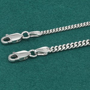May include: A silver curb chain necklace with a lobster clasp closure. The chain is made of small, interlocking links.