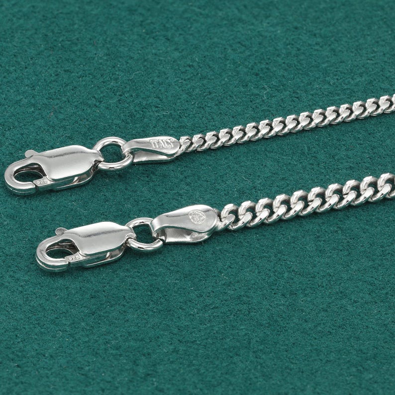 May include: A silver curb chain necklace with a lobster clasp closure. The chain is made of small, interlocking links.