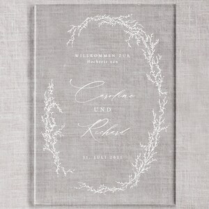 May include: A white wedding invitation with a floral wreath design. The text reads "Willkommen zur Hochzeit von Caroline und Richard 31. Juli 2021".