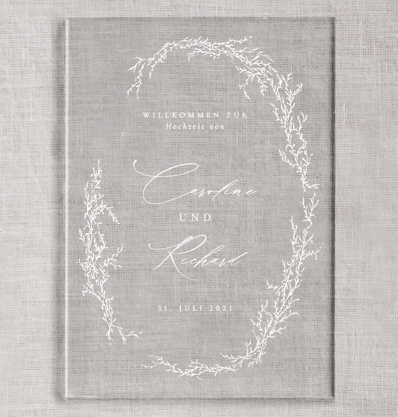 May include: A white wedding invitation with a floral wreath design. The text reads "Willkommen zur Hochzeit von Caroline und Richard 31. Juli 2021".