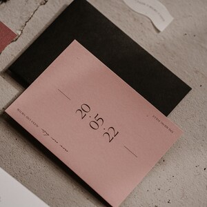 May include: A blush pink card with the date "0.15.22" printed in black ink. The card is on a light grey textured surface.
