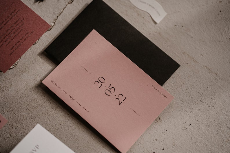 May include: A blush pink card with the date "0.15.22" printed in black ink. The card is on a light grey textured surface.