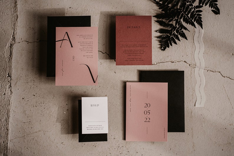 May include: A set of wedding invitations printed on black and pink card stock. The invitations feature a minimalist design with a black script font and the text "AND" and "RSVP". The date "20.05.22" is printed on a separate card.