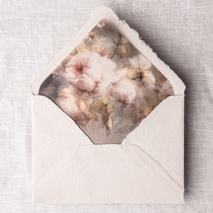 May include: A white envelope with a floral design on the front. The design features a watercolor painting of pink and brown flowers.