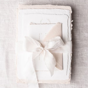May include: A stack of white and cream paper stationery with a white ribbon tied around it. The top sheet has the initials "C&R" in a circle with a floral design. The text "Ich komme zu dir" is visible on the second sheet.