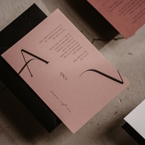 May include: A pink wedding invitation with black calligraphy lettering. The invitation includes the text "Wir laden Euch herzlich zu unserer Hochzeit am 20.05.22 in Bergisch Gladbach. Bitte seid um 11 Uhr im Bergischen Hof. Nach der Trauung wollen wir feiern mit Euch.  [Name] und [Name] Wir freuen uns auf Euch."