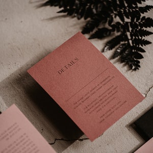 May include: A red card with the word "DETAILS" printed in black. The card has text about a wedding ceremony and reception, including the date, time, and location.