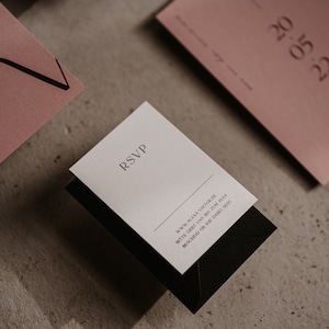 May include: A white RSVP card with black text and a black envelope. The text on the card reads "RSVP" and includes a website address and a request to RSVP by a certain date.