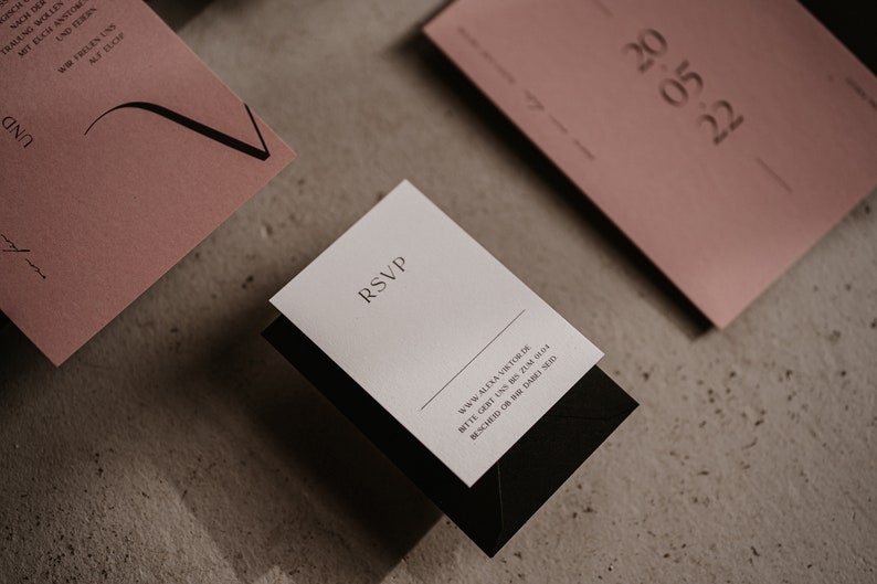 May include: A white RSVP card with black text and a black envelope. The text on the card reads "RSVP" and includes a website address and a request to RSVP by a certain date.