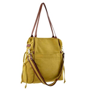 Pode incluir: Uma bolsa tote de lona amarela mostarda com al&ccedil;as de couro marrom e uma al&ccedil;a de ombro de couro marrom. A bolsa tem um bolso com z&iacute;per na frente e um fecho de cord&atilde;o na parte superior.
