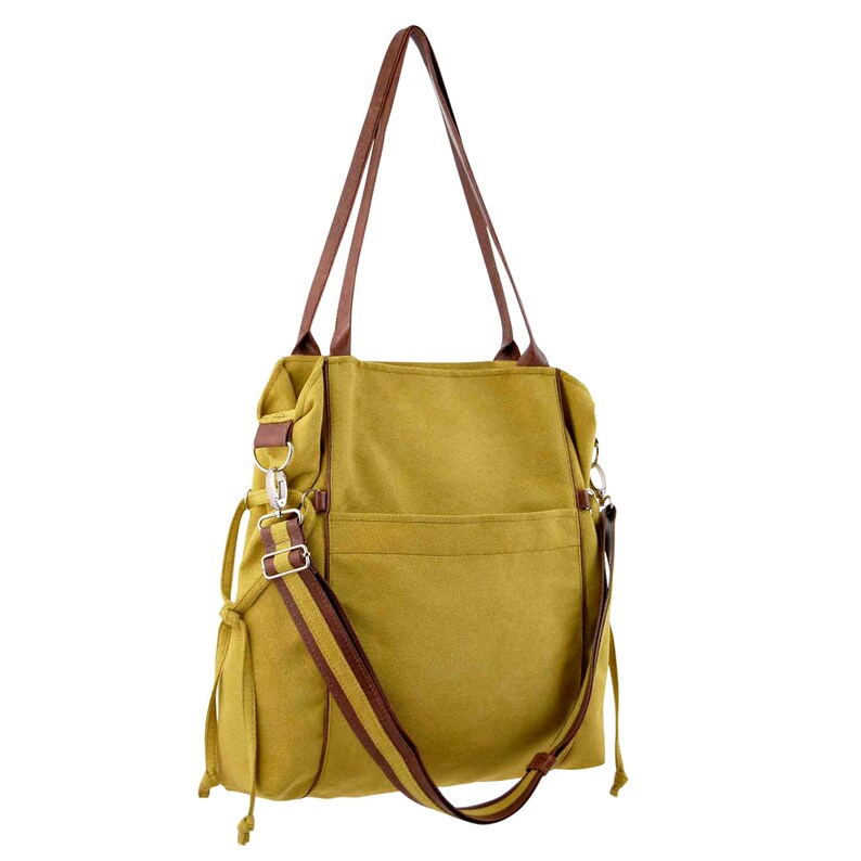 Pode incluir: Uma bolsa tote de lona amarela mostarda com al&ccedil;as de couro marrom e uma al&ccedil;a de ombro de couro marrom. A bolsa tem um bolso com z&iacute;per na frente e um fecho de cord&atilde;o na parte superior.