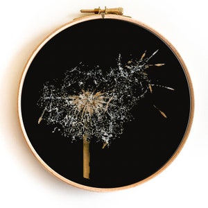 May include: A close-up of a dandelion seed head with white seeds and a brown stem against a black background. The dandelion is in a round wooden embroidery hoop.