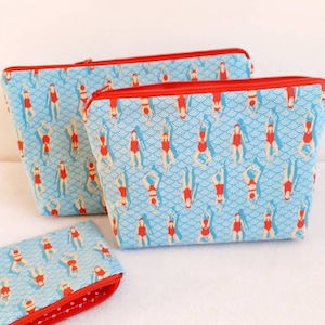 Könnte beinhalten: Drei Reißverschlusstaschen mit blauem Hintergrund und einem Muster aus roten Frauen in Badeanzügen. Die Taschen sind mit rotem Stoff mit weißen Punkten gefüttert.