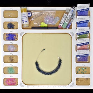 Organized workspace of the Acclaim Crafts Seed Beaders Dream Board holding beading wax, needles, seed beads, and a bracelet.